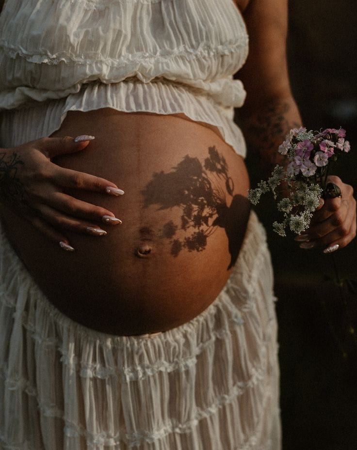 Close up of pregnant belly with wildflower shadow, mother holding flowers